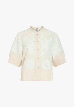 Chemise beige à manches courtes avec boutons, broderie florale blanche, col rond et coupe ample et carrée.