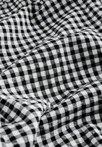 Tissu vichy noir et blanc avec un motif à carreaux, montrant une texture douce et un aspect froissé.
