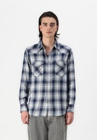 Camicia di flanella a quadri blu e bianchi con due tasche sul petto, maniche lunghe e chiusura con bottoni. Tessuto morbido e vestibilità comoda.