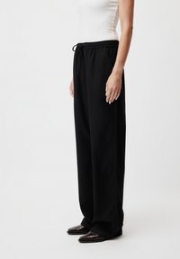 Pantaloni neri a gamba larga realizzati in un materiale morbido, con cintura elastica e cordino e una consistenza liscia.