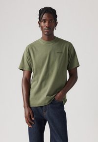 Tricou din bumbac de culoare verde măsliniu, cu o croială lejeră, guler rotund și mâneci scurte. Prezintă un logo discret "Levi's" pe piept.