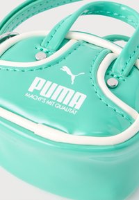 Γυαλιστερή τυρκουάζ τσάντα χειρός Puma με λευκή επένδυση και ασημένιες τρούκ, με το λογότυπο Puma και το κείμενο "MACHT'S MIT QUALITÄT".