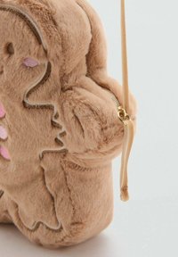 Hladká béžová crossbody taška tvarovaná ako perníkový sušienka s ružovými a hnedými vyšívanými detailmi a béžovým popruhom so zipsom.