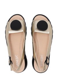 Metalické zlaté ploché boty s černými podrážkami. Mají kulatý černý akcent, otevřenou špičku a slingback design. Hladký povrch se švy.
