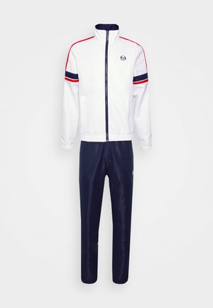 White athletic jacket with red and navy stripes, zip closure, and high collar. Paired with navy trousers featuring a small logo detail.
