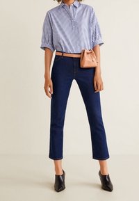 Chemise à manches courtes rayée bleu et blanc avec col, associée à un jean court bleu foncé et des chaussures noires à bout pointu. Petit sac à main beige.