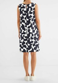 Šaty bez rukávů v námořnické modři a bílé s abstraktním vzorem. Mají zadní detail ve tvaru klíčové dírky a rovný střih, sahající těsně nad kolena.