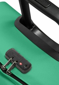 Grön mjuk resväska med en strukturerad yta, svart teleskophandtag och TSA-godkänd lås med silverfärgade dragkedjor.