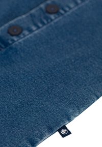 Tessuto di denim blu scuro con una finitura testurizzata, dotato di due bottoni neri e una piccola etichetta con logo sul bordo.