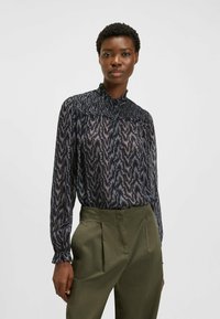 Blusa scura stampata con collo alto, dotata di yoke arricciato, maniche lunghe e un motivo floreale nelle tonalità di blu navy e viola.