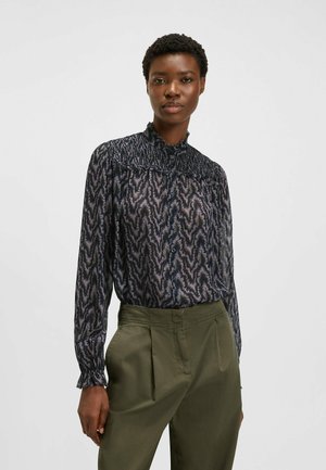Blusa scura stampata con collo alto, dotata di yoke arricciato, maniche lunghe e un motivo floreale nelle tonalità di blu navy e viola.