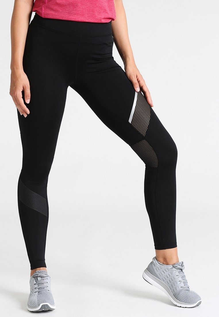 Černé sportovní legíny s vysokým pasem, s texturovanými síťovinovými detaily a bílým pruhováním po stranách. V páru se šedými běžeckými botami.