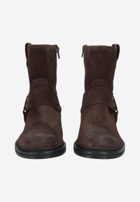Bottines en suède marron avec un bout rond, des zips latéraux et une sangle décorative avec des clous en métal. Semelles en caoutchouc noir avec des détails de couture.