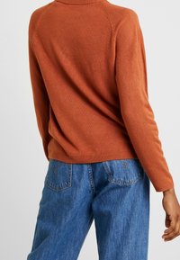 Maglione lavorato a maglia color ruggine con un colletto rotondo e maniche raglan, abbinato a jeans in denim blu a vita alta.
