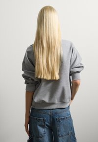 Grijze sweatshirt met verlaagde schouders en geribbelde cuffs, gecombineerd met blauwe denim cargo shorts met grote achterzakken. Lang, steil blond haar.