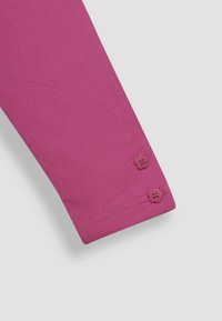 Fuchsias långärmad skjorta med en slät textur, två blomformat knappar vid manschetten och en enkel, figurnära design.