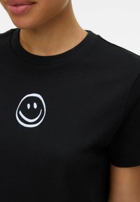 Zwarte katoenen t-shirt met ronde hals, voorzien van een witte geborduurde glimlachende gezicht op de borst. Glad textuur, korte mouwen.