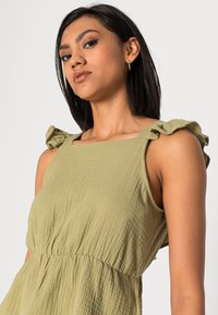 Vestido verde oliva, texturizado, com detalhes de ombros franzidos e decote quadrado. Design de cintura império para um ajuste relaxado.