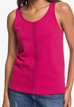 Femme portant un haut sans manches rose vif avec une rayure texturée verticale à l'avant, associée à un jean bleu.