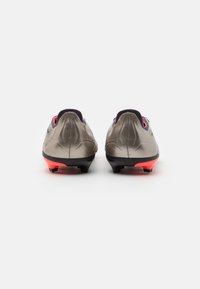 Scarpe da calcio con tomaia grigio metallico, suola nera e dettagli rosso brillante. Presentano un design elegante e allungato con una parte posteriore testurizzata.