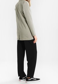 Szara koszulka w kratę z długim rękawem, luźnego kroju, noszona z czarnymi spodniami o szerokich nogawkach. Obuwie: czarne trampki z białą podeszwą.