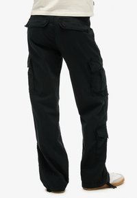 Zwarte cargo-broek met meerdere zijzakken, een ontspannen pasvorm en een duurzame stof. Accenten met een flapdetail op de achterzak.