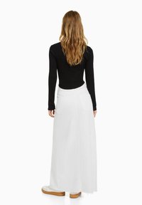 Valkoinen pitkä farkkuhame, jossa on revitty helma ja takataskut, yhdistetty mustaan tiukkaan toppiin. Malli näkyy takaa.