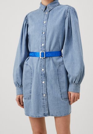 Spijkerjurk met een knoopsluiting aan de voorkant, opgeblazen lange mouwen, voorzakken en een blauw merkriempje, met een lichtblauwe wassing en een gladde textuur.