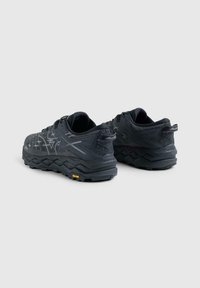 Un paio di scarpe da trail running nere Mizuno con tomaia a motivo, suole spesse e testurizzate, e logo Vibram sulla suola esterna.