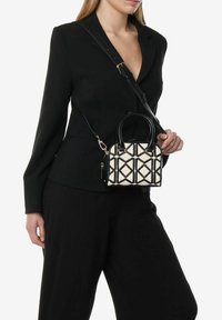 Zwarte en crèmekleurige handtas met diamantenpatroon, gestructureerde vorm, dubbele handvatten, afneembare schouderriem en gouden hardware accenten.