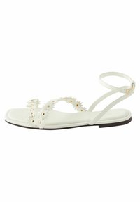 Weiße flache Sandalen mit floralen Verzierungen und goldfarbener Hardware. Sie verfügen über eine glatte Textur und einen einzelnen verstellbaren Knöchelriemen.