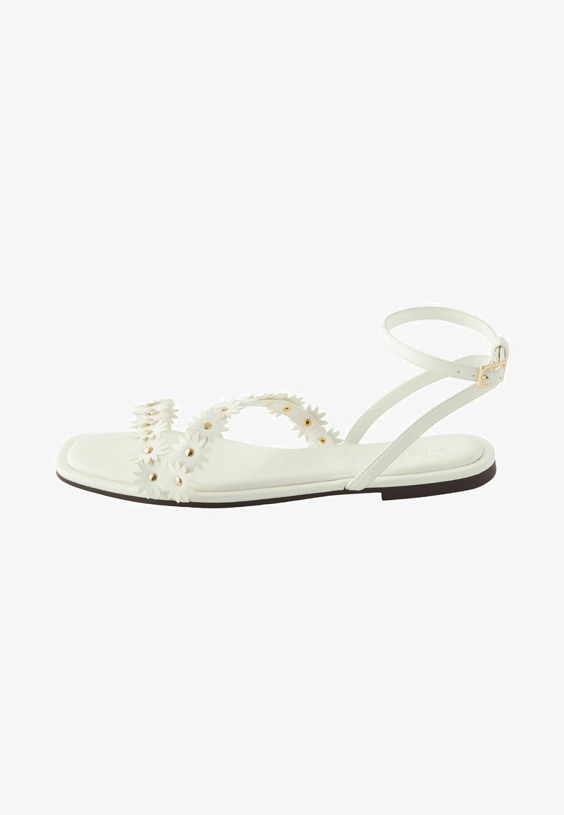 White flat sandals feature floral embellishments and gold-tone hardware. They have a smooth texture and a single adjustable ankle strap.