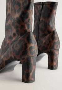 Bottines à imprimé léopard marron et noir avec une finition texturée, des zips sur le côté et un talon épais. Présente des lignes élégantes et une conception durable.