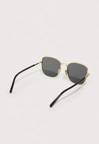 Ruutujalaläätsed tumedate läätsedega, kuldse metallraami ja musta plastist templiga. Omavad minimalistlikku disaini ja kerget konstruktsiooni.