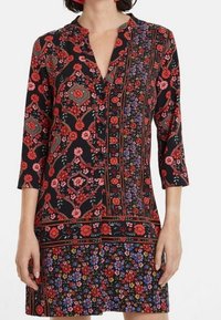 Šaty s květinovým vzorem, které mají červené, růžové a modré květy na černém pozadí. Tříčtvrteční rukávy a zapínání na knoflíky.