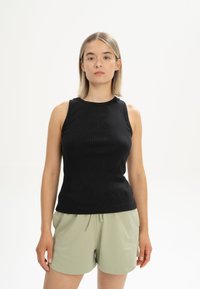 Schwarzes geripptes Tanktop mit Rundhalsausschnitt, ärmellosem Design und figurbetontem Schnitt, kombiniert mit hellgrünen Shorts mit Kordelzug.