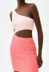 En axelbandslös räfflad crop top i ljusrosa som matchas med en räfflad minikjol i korallrosa; båda har en slät textur och en figurnära design.