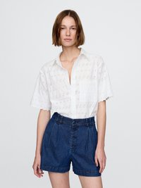 Hvit kortermet skjorte med knapp og broderi i øyeform, samt en brystlomme, kombinert med mørkeblå denim høytlivshorts med frontknapper.