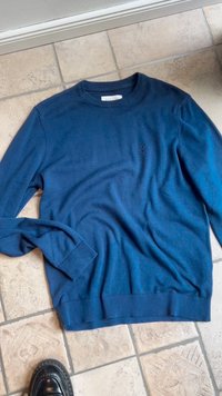 Sweater de malha azul marinho com decote redondo, punhos e bainha canelados; apresenta um pequeno logotipo no peito; textura suave.