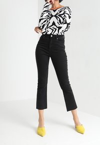 Svarta högmidjade jeans med utfläkt vrist, kombinerat med en svartvitrandig zebra-mönstrad tröja och gula spetsiga klackskor.