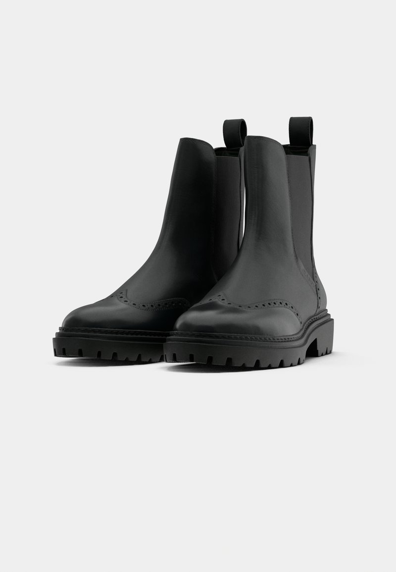 Schwarze Leder-Ankle-Boots mit elastischen Seitenpartien, abgerundetem Zehenbereich, Brogue-Dekoration und chunky, strukturiertem Gummisohle.