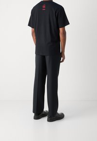 Mustat puuvillateepaidat, joissa on lyhyet hihat, punaisella tekstillä takana, yhdistettyinä löysiin mustiin housuihin ja mustiin kenkiin.