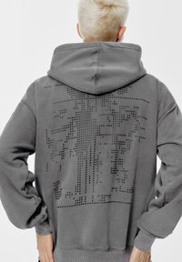 Szara bluza z kapturem z miękkiego materiału. Posiada punkcikowy wzór na plecach, ściągacze przy mankietach oraz luźny krój.