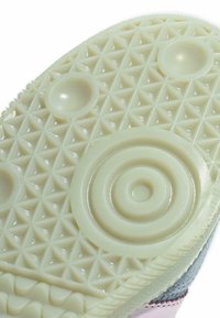 Potplat cipela s teksturiranim trokutastim uzorkom, kružnim zonama za prianjanje i uzdignutim dijelovima za vuču i potporu na svjetloj gumenoj površini.