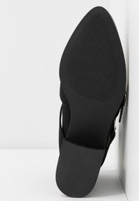 Scarpa con tacco nera con tomaia liscia e suola in gomma texturizzata, caratterizzata da una punta affusolata e un tacco sottile per un'elevazione aggiuntiva.