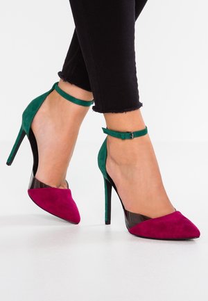 Czółenka na wysokim obcasie z zielonym zamszowym tyłem, fuksjowym zamszowym przodem i przezroczystymi panelami bocznymi. Posiadają pasek wokół kostki i szpiczasty czubek.