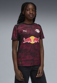 Rød og sort kortærmet fodboldtrøje med geometrisk mønster, der har et gult Red Bull-logo og Puma-logo på brystet.