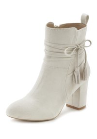 Stivale alla caviglia in suede beige con punta affusolata, zip sul retro, dettaglio annodato alla caviglia e piccole frange. Presenta un tacco spesso.