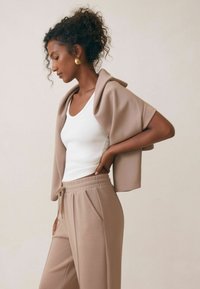 Beige sweatshirt over een witte tanktop, gecombineerd met beige joggers. De stof is soepel, met een elastische tailleband en zijzakken.