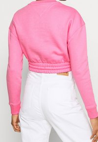 Felpa rosa corta con vita a costine e maniche lunghe, abbinata a pantaloni bianchi a vita alta con tasche posteriori.